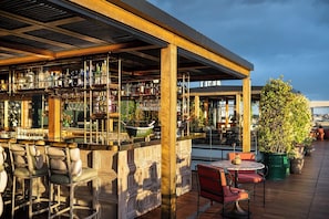 An outdoor bar area with a wooden structure, seating, and a variety of bottles and glasses.