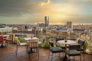 A rooftop terrace with outdoor seating, a cityscape view, and a sunset.