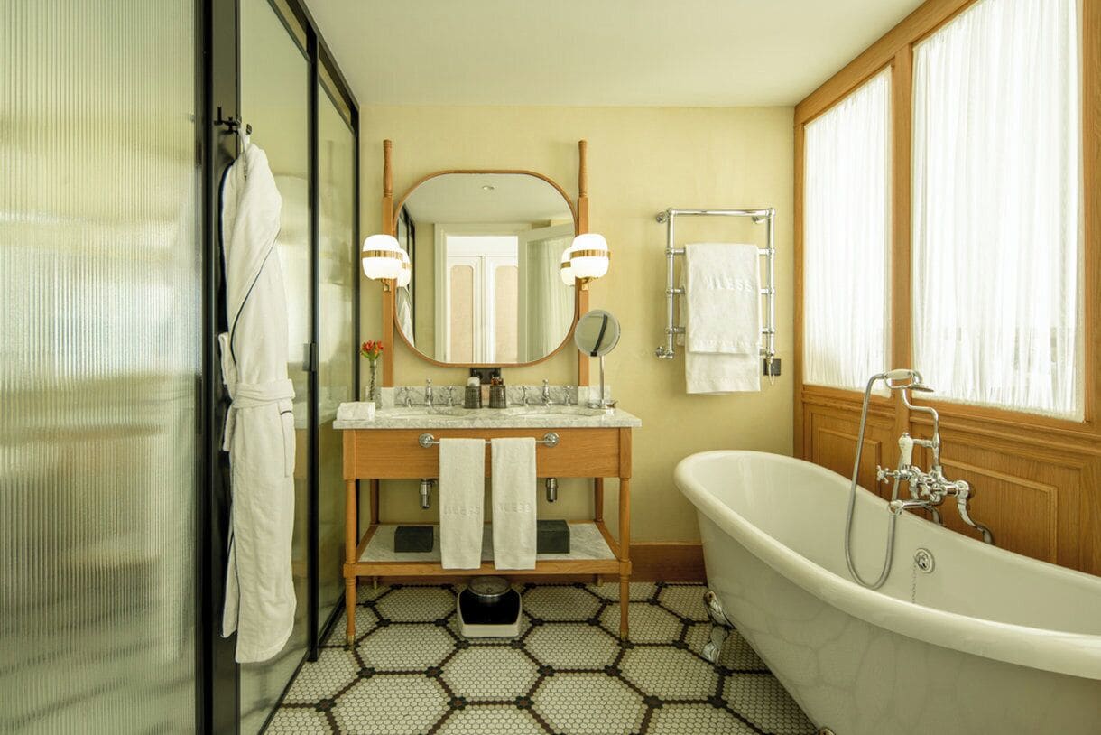 Un baño con una bañera independiente, un tocador con espejo y dos luces, un perchero y una ventana con cortinas.
