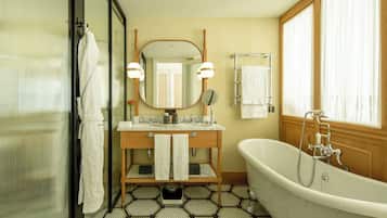 Un baño con una bañera independiente, un tocador con espejo y dos luces, un perchero y una ventana con cortinas.