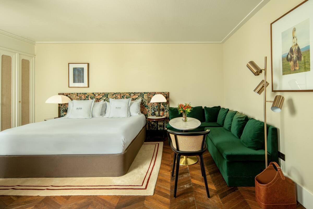 A hotel room with a large bed, a green sofa, a small table with a vase, and a framed picture on the wall.