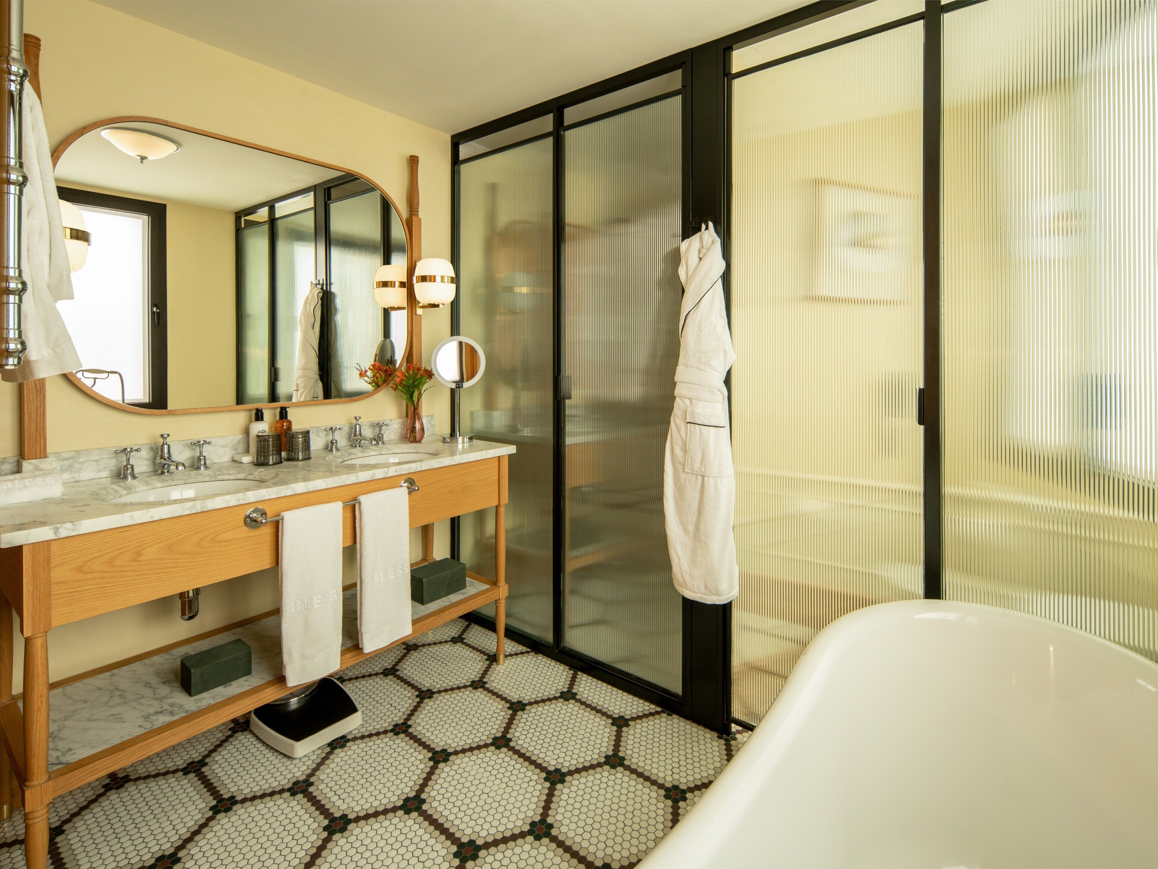 Un baño moderno con un espejo grande, dos lavamanos, una bañera y piso de baldosas.
