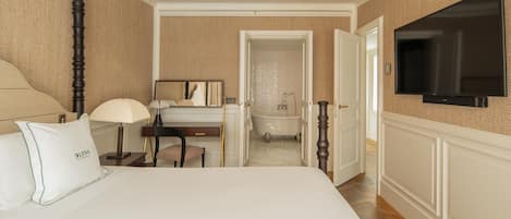 Habitación de hotel con cama, escritorio, silla, lámpara y televisor montado en la pared.