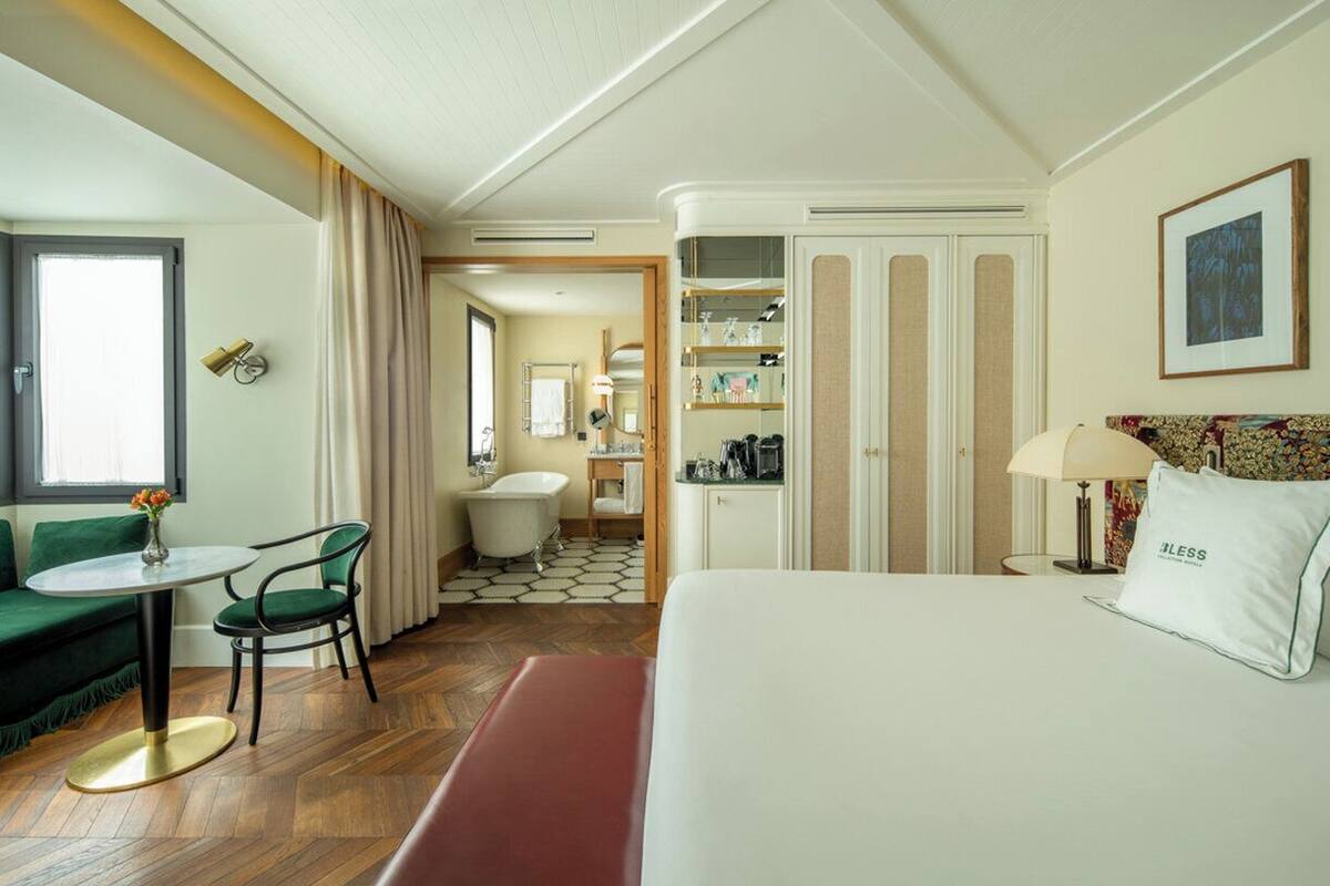 A hotel room with a bed, a desk, a chair, a sofa, a bathroom, and a wardrobe.