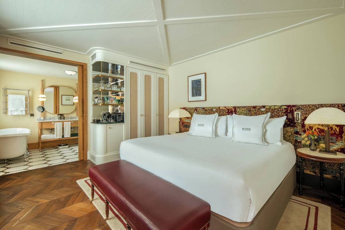 A hotel room with a large bed, a red bench, a bathroom with a bathtub, and a wardrobe.