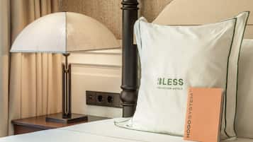 Una cama de hotel impecable con un cojín que dice 'Bless Collection Hotels' y un folleto titulado 'Hogsty System'.