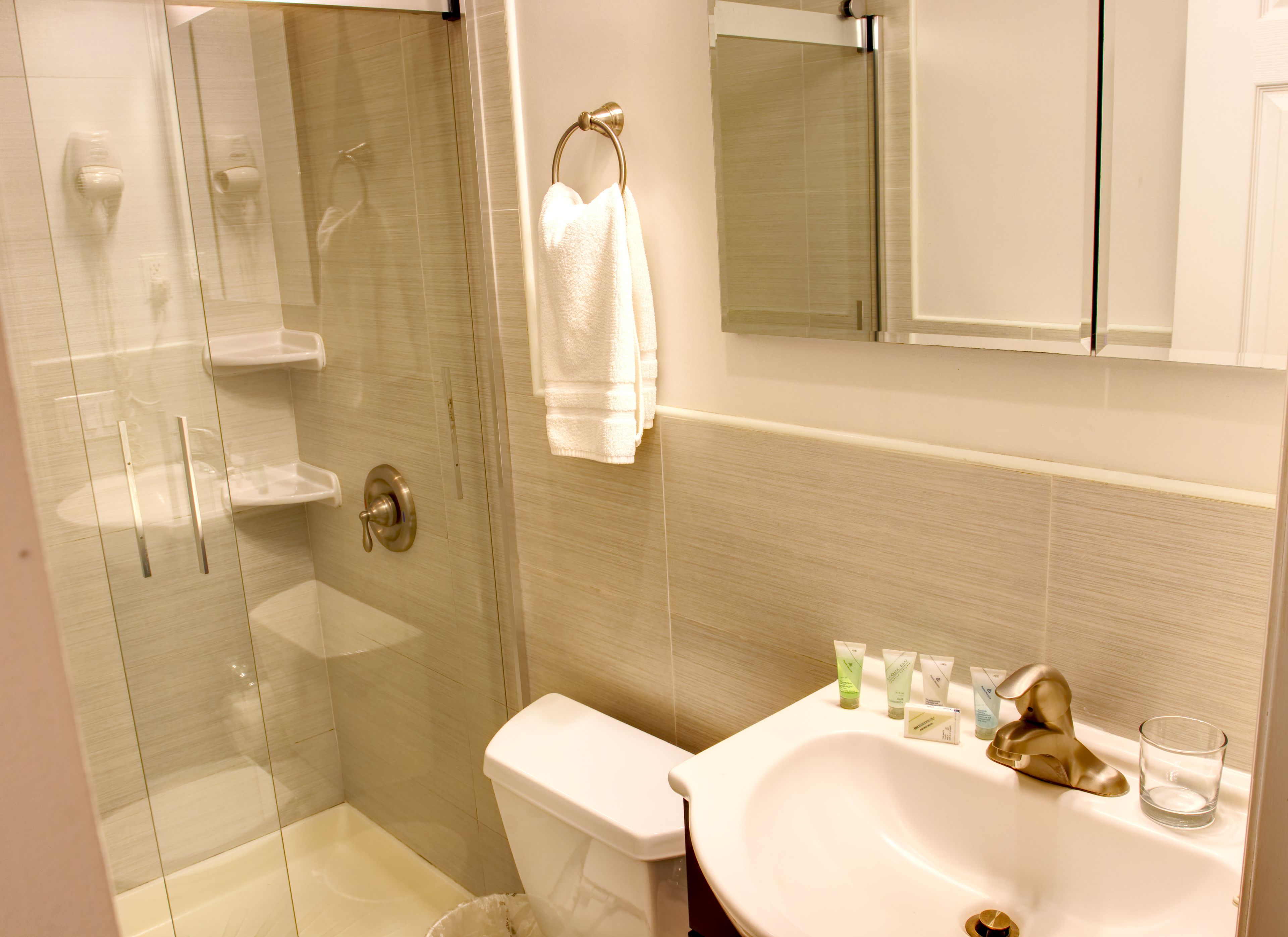 Une salle de bain avec une douche à parois de verre, des toilettes, un lavabo avec des articles de toilette et un porte-serviettes.