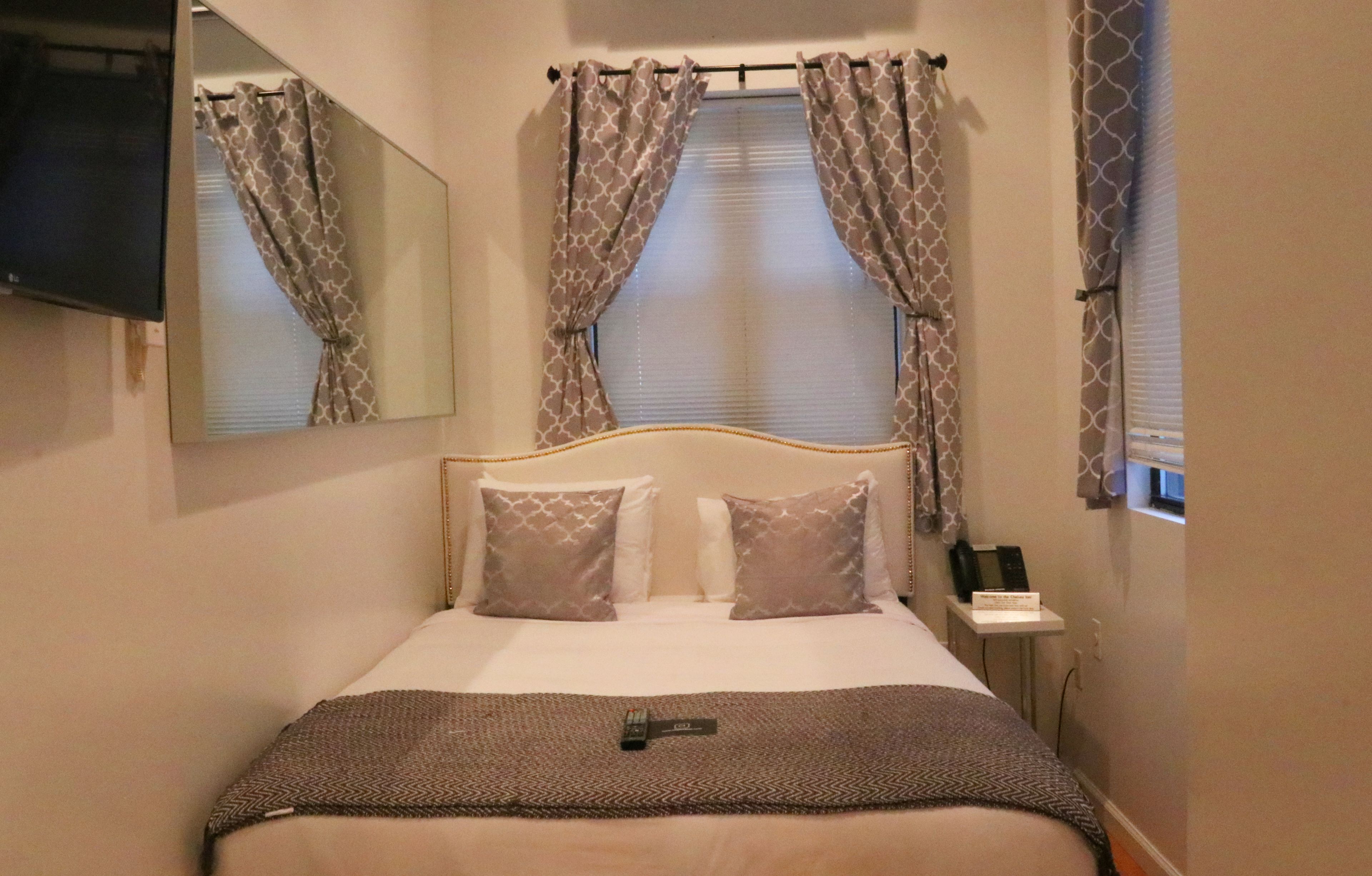 A hotel room with a bed, a bedside table with a phone, and a TV mounted on the wall.