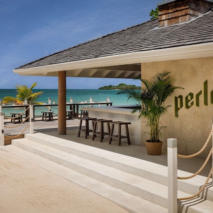 A beachside restaurant with outdoor seating, a wooden deck, and a view of the ocean.