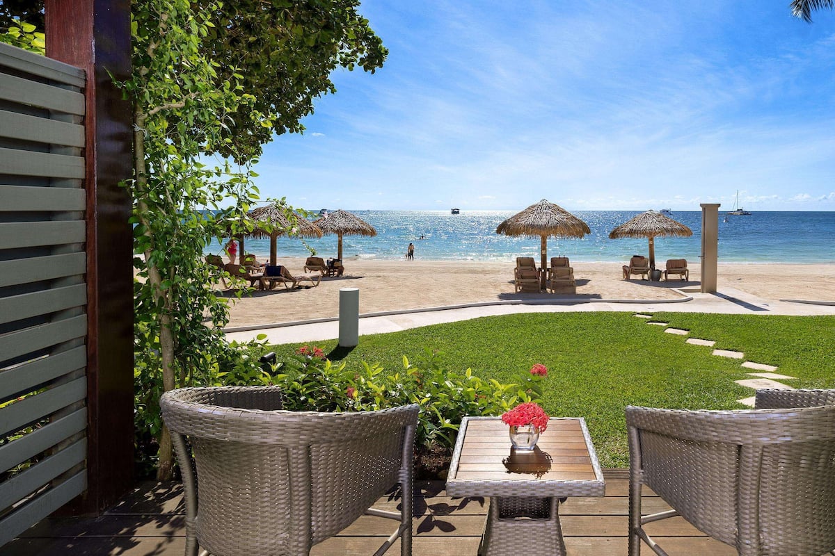 Un patio con mobiliario de mimbre, una mesa con un florero y vista a la playa y el océano.