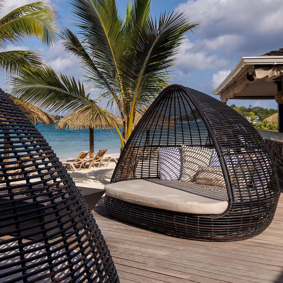A beachside lounge area with wicker chairs and a thatched-roof structure.