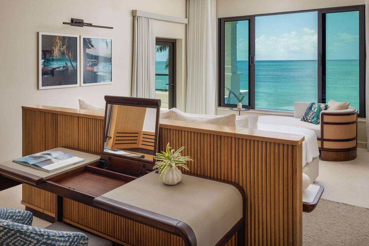 Habitación de hotel con cama, escritorio, silla, televisor y vista al océano.