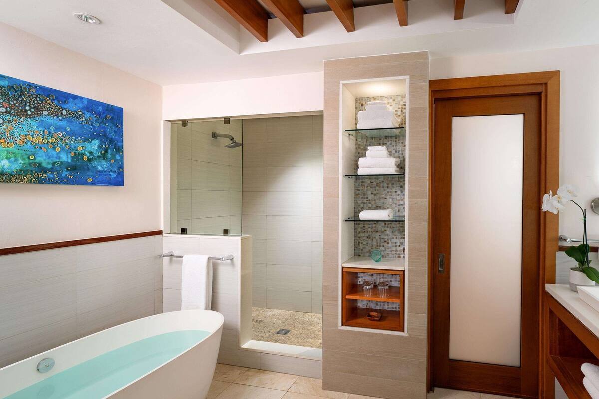 Un baño moderno con ducha de vidrio, un espejo grande y un estante empotrado con toallas.