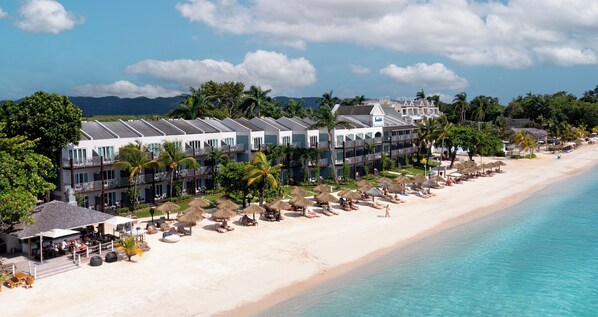 A beachfront hotel with multiple-story buildings, a sandy beach, and thatched umbrellas. - Sandals Negril - ALL INCLUSIVE Adults Only (Negril)