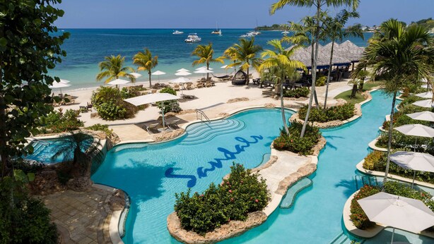 A resort pool with 'Sandals' written in the water, surrounded by palm trees, beach chairs, and umbrellas. - Sandals Negril - ALL INCLUSIVE Adults Only (Negril)