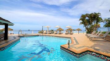 A pool with a seahorse decoration, lounge chairs, umbrellas, and a view of the ocean.