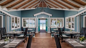 A dining area with wooden tables and chairs, a view of the beach through open doors, and a ceiling with wooden beams. - Sandals Negril - ALL INCLUSIVE Adults Only (Negril)