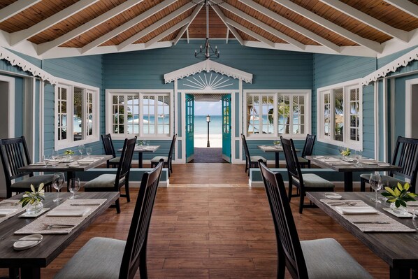 A dining area with wooden tables and chairs, a view of the beach through open doors, and a ceiling with wooden beams. - Sandals Negril - ALL INCLUSIVE Adults Only (Negril)