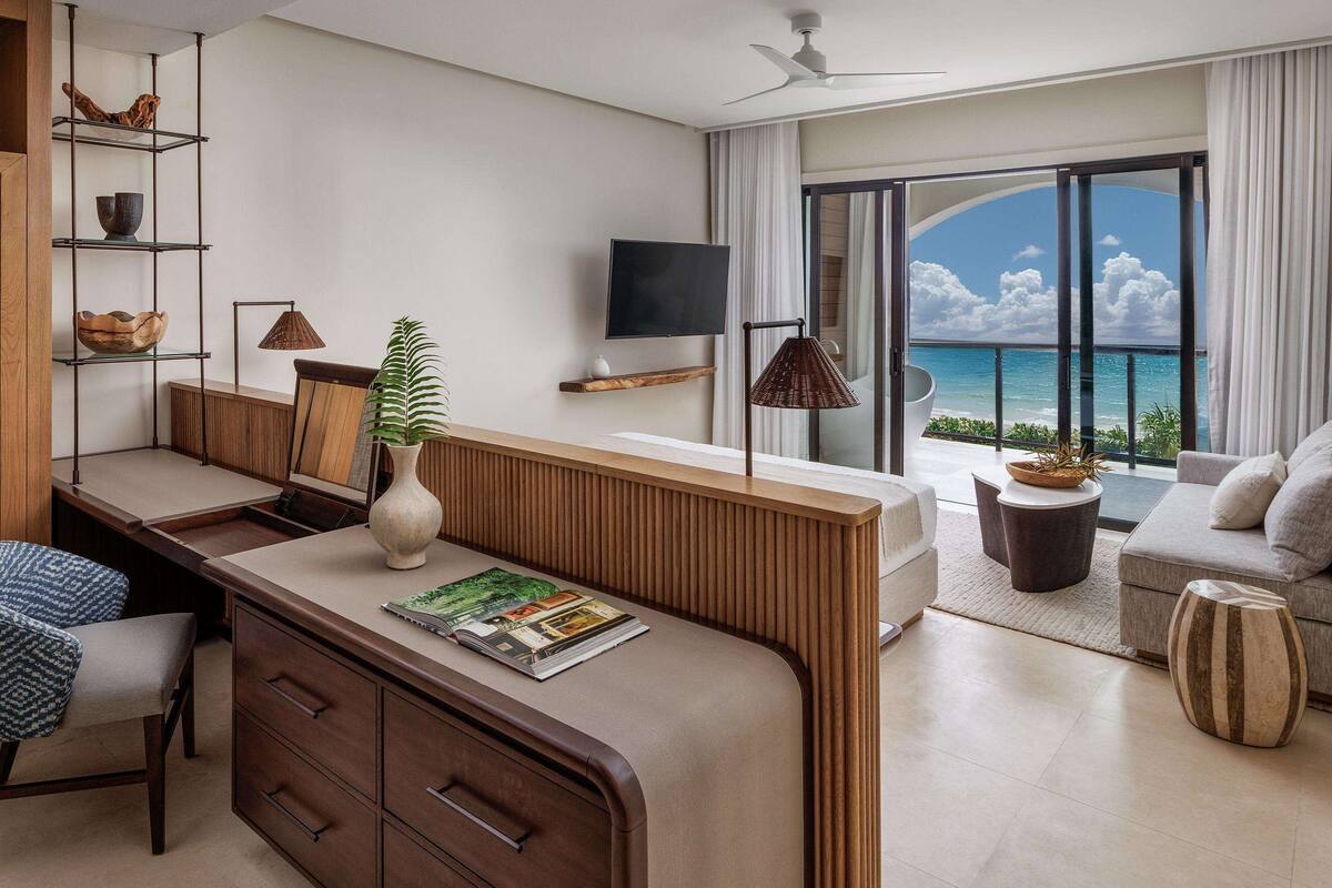 Una habitación de hotel moderna con un escritorio de madera, un sofá cómodo, un televisor y un balcón con vistas al océano.