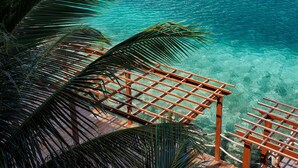 Una terraza de madera con vista a aguas turquesas cristalinas y palmeras.