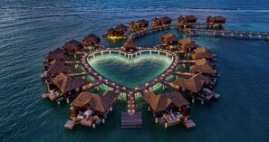 Un complexe hôtelier construit sur pilotis, avec des bungalows aux toits de chaume disposés en forme de cœur et reliés par des passerelles au-dessus de l’eau.