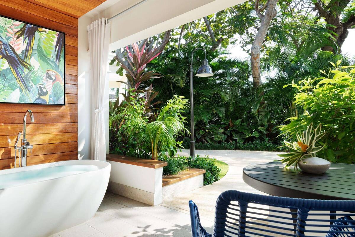 Une salle de bain moderne avec une baignoire sur pieds, un lambris en bois et un grand tableau aux motifs tropicaux.