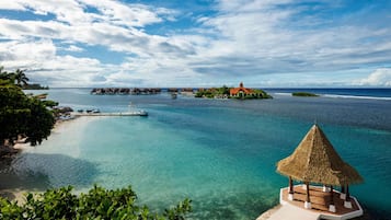 A tropical beach with clear turquoise waters, a thatched-roof gazebo, and overwater bungalows.