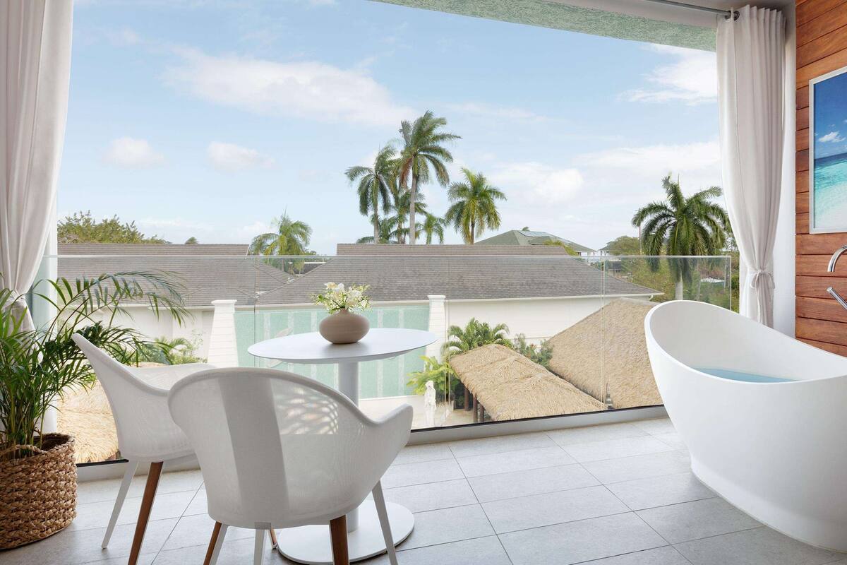 Une salle de bain moderne avec une baignoire sur pieds, une table ronde avec des chaises et une vue sur un paysage tropical.