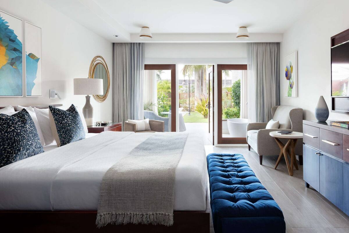 Une chambre d’hôtel avec un grand lit, un banc bleu, une télévision et une vue sur l’extérieur.