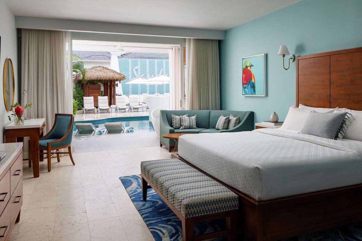 Une chambre d’hôtel avec un grand lit, un bureau avec une chaise, un canapé, une petite table et une vue sur l’espace piscine.