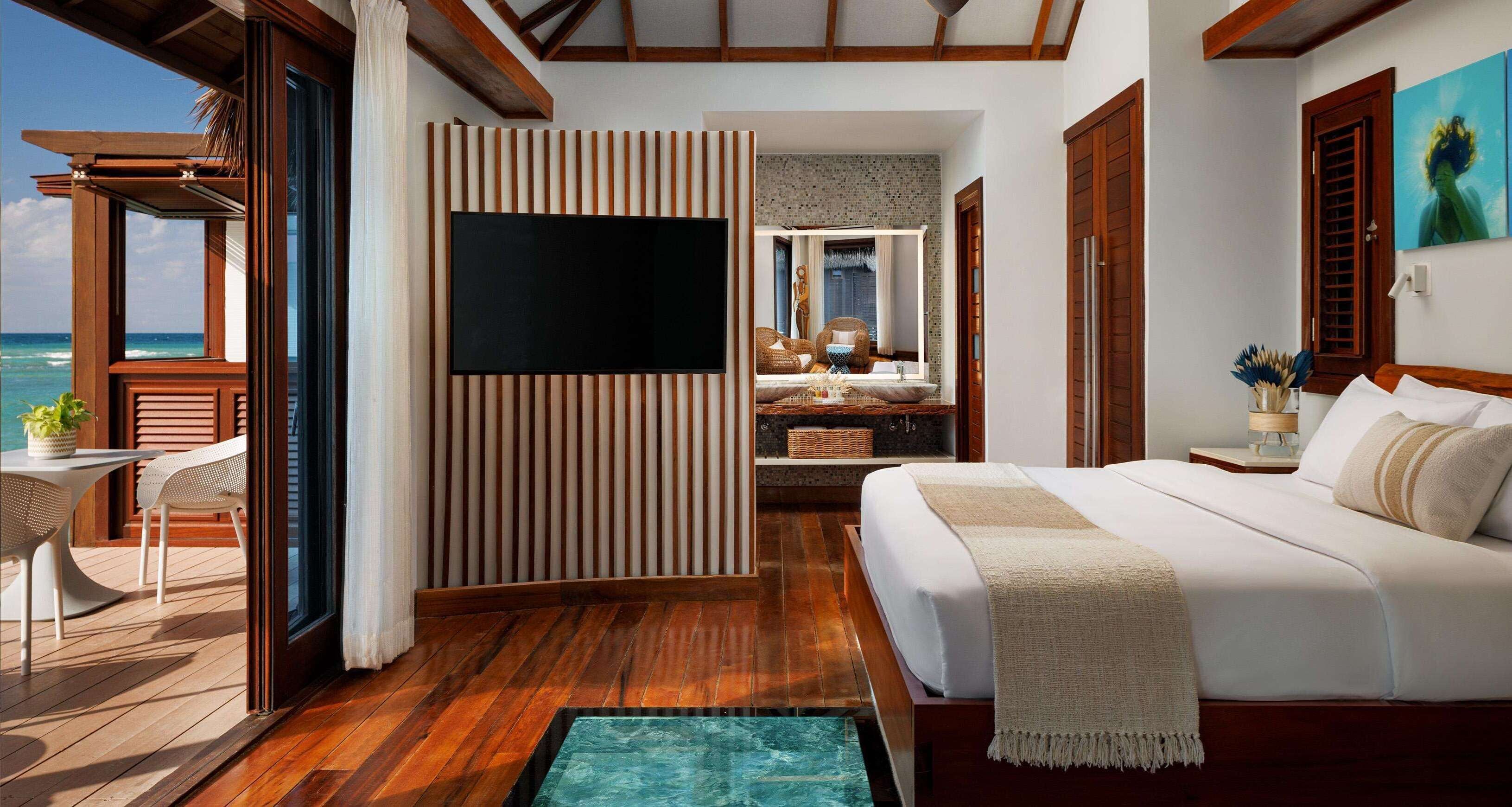 A spacious room with a large bed, a TV, a small table with chairs, a view of the ocean, and a bathroom with a bathtub.