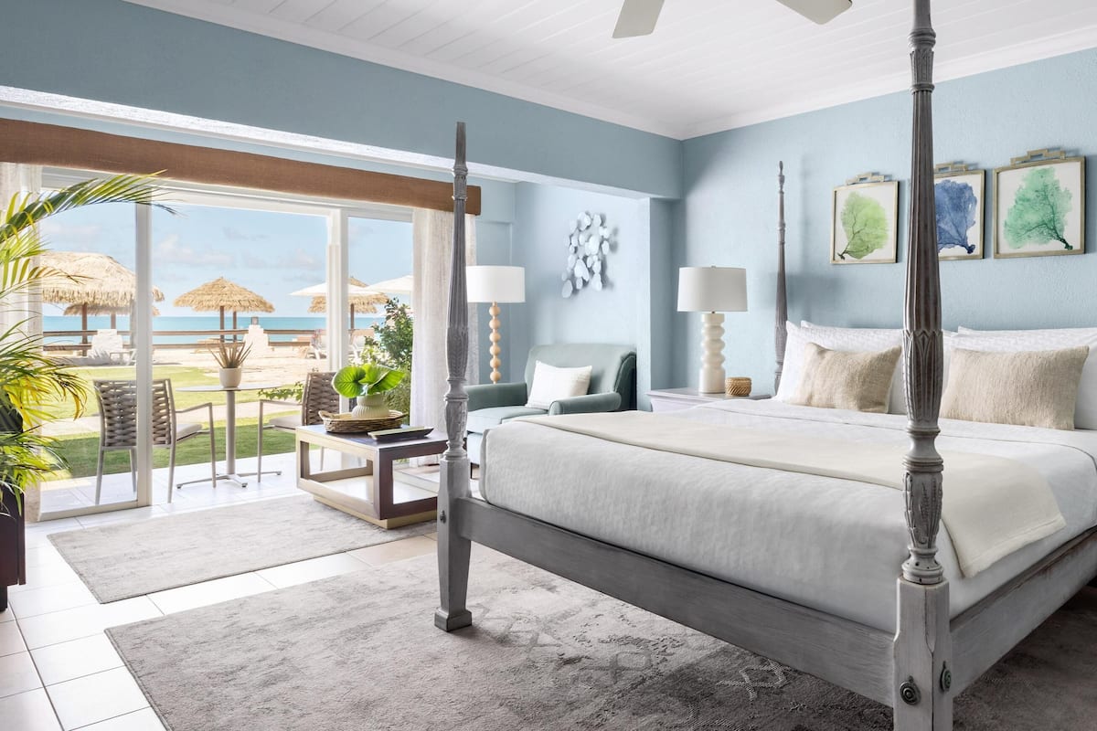 Une chambre dotée d’un lit à baldaquin, d’un balcon offrant une vue sur la plage et d’un coin repas avec une table et des chaises.