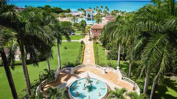 A resort with a central fountain, palm trees, and a view of the ocean.