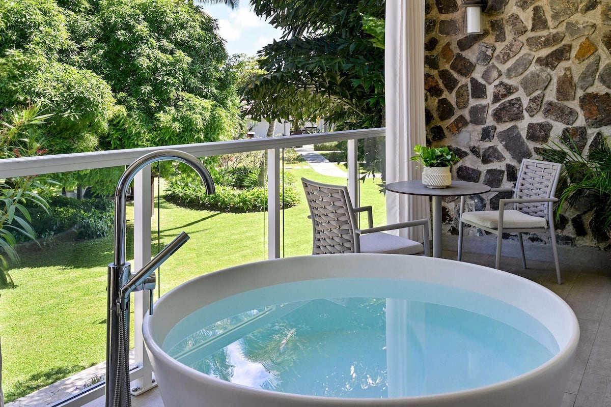 A spa area with a large oval hot tub, a stone wall, and a view of a lush garden.