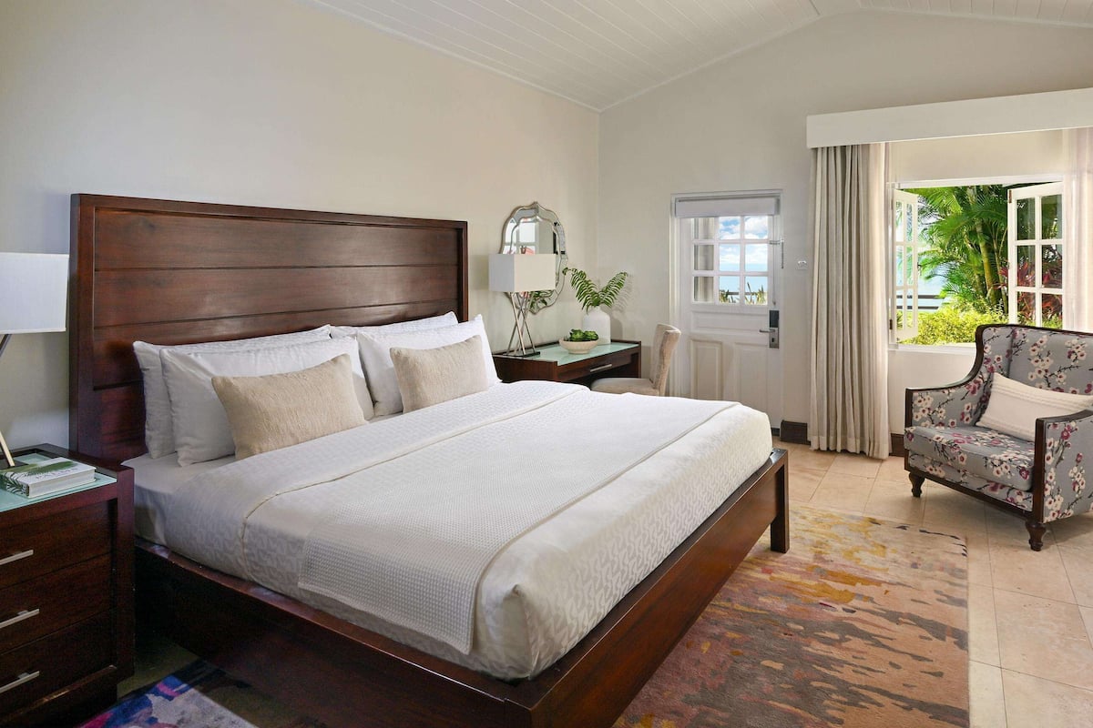 A hotel room with a large bed, a chair, a desk with a lamp, a TV, and a window with curtains.