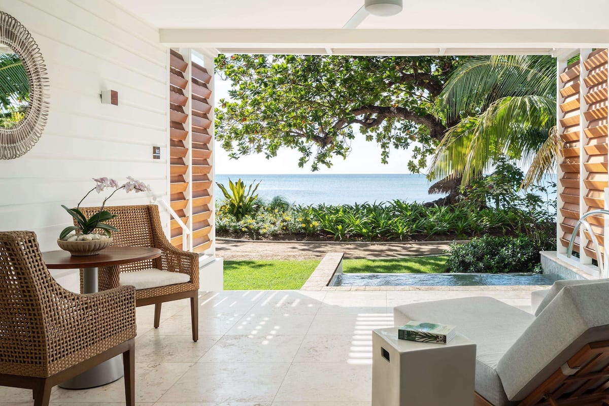A room with a view of the sea, wicker furniture, and a small garden area.