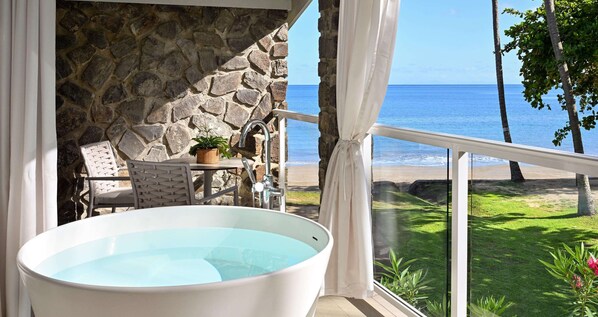 Un baño con paredes de piedra, una bañera, una mesita con una planta y una silla.