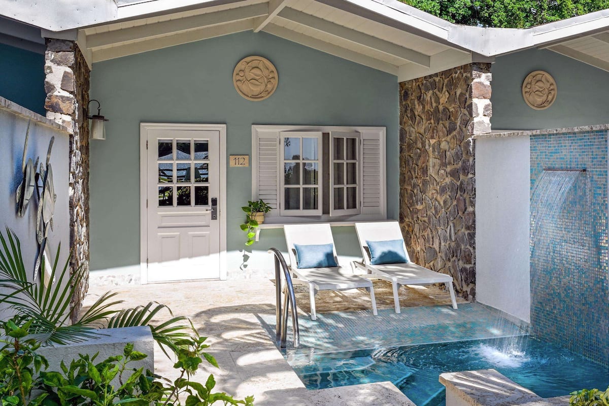 A pool area with two white lounge chairs and a stone wall.