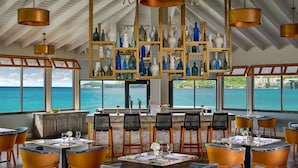 A restaurant with a view of the sea, featuring a bar area, dining tables, and chairs.