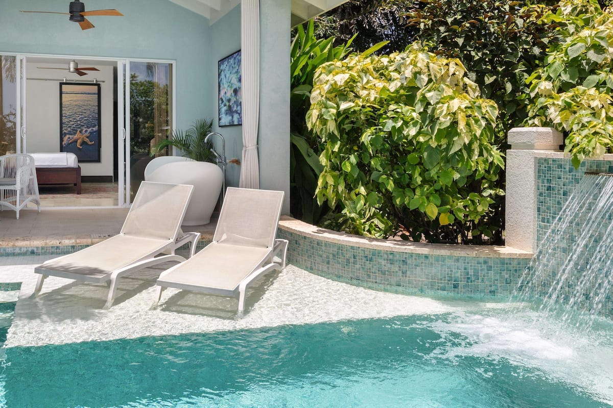 A pool area with lounge chairs, a table, and a view of the outdoors.