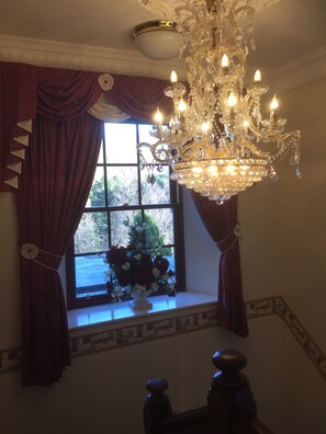 A room with a large window, a chandelier, and a vase with flowers on the windowsill. - Glenspean Lodge Hotel (Roybridge)