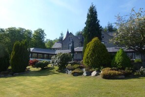 A large stone building with a steeply pitched roof, surrounded by well-maintained lawns and various types of trees. - Glenspean Lodge Hotel (Roybridge)