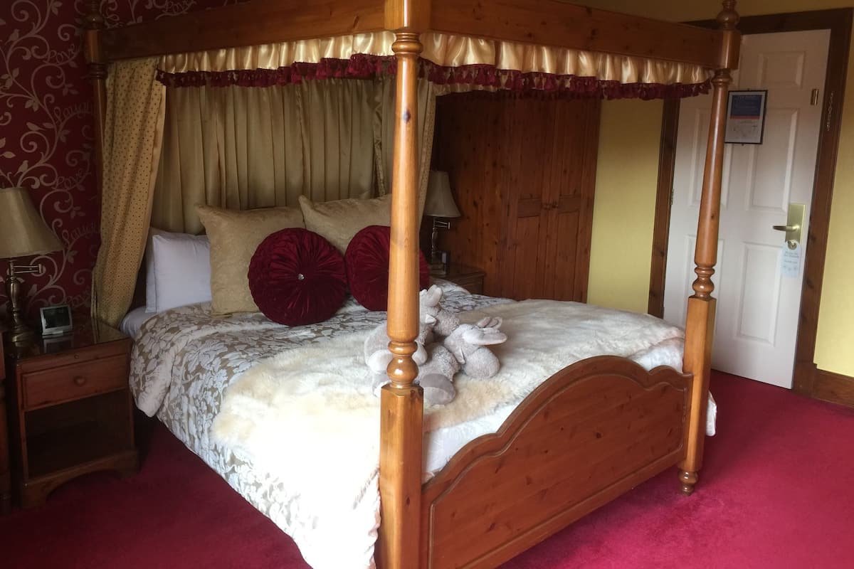 A four-poster bed with a floral bedspread, two red pillows, and a fluffy white comforter.