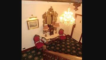 A room with a wooden staircase, a chandelier, a mirror, and two chairs.