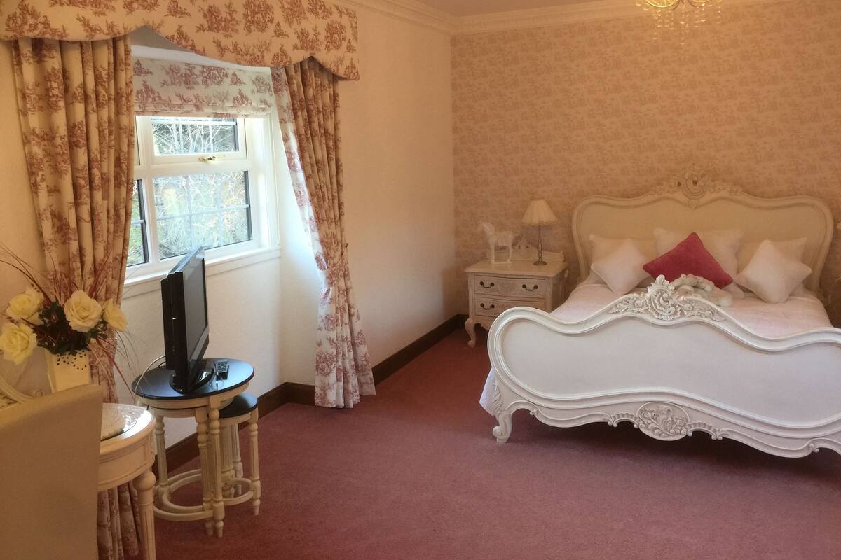A bedroom with a bed, nightstand, lamp, and a desk with a computer.