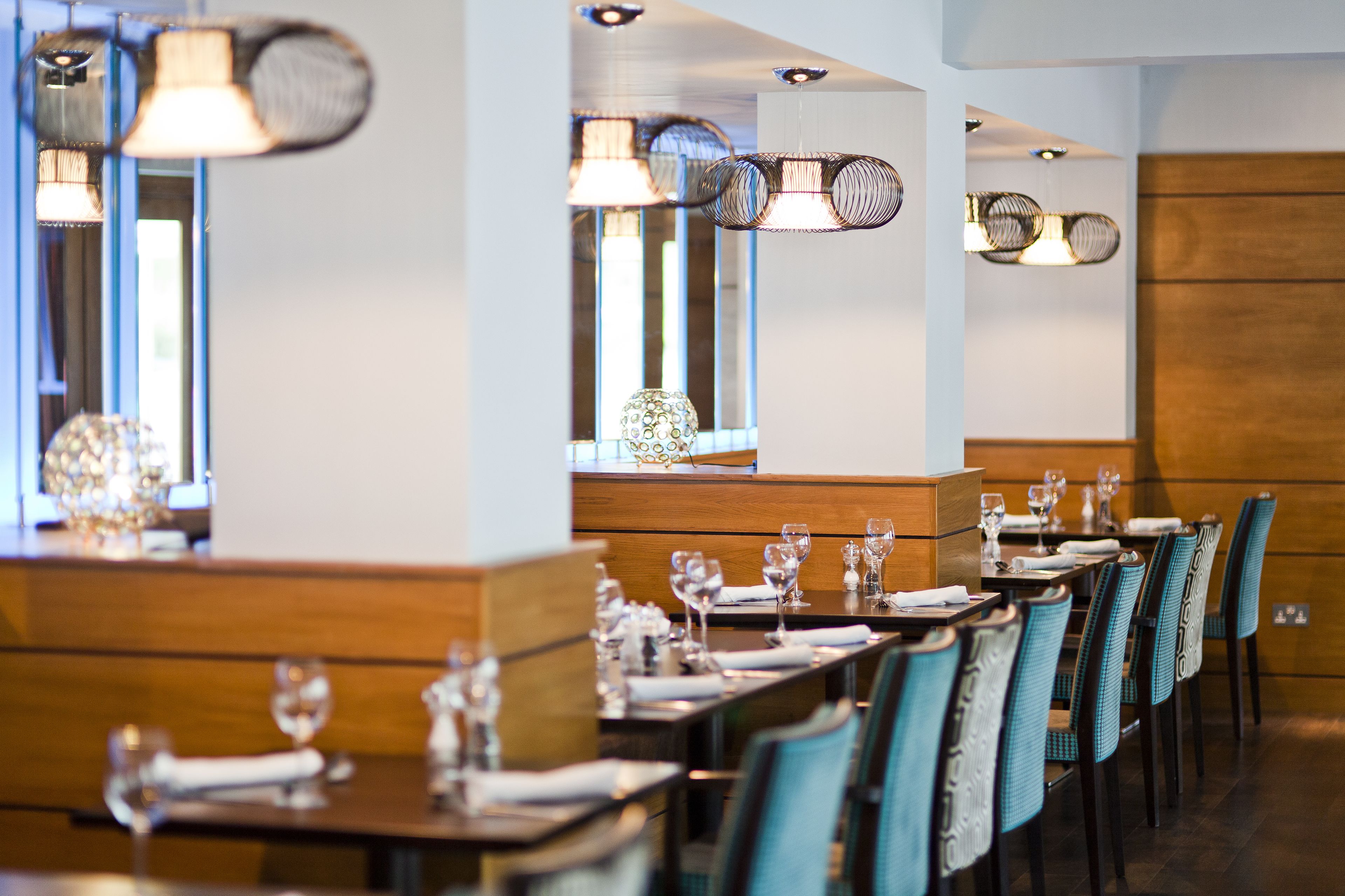 A restaurant with long tables, chairs, and hanging pendant lights.