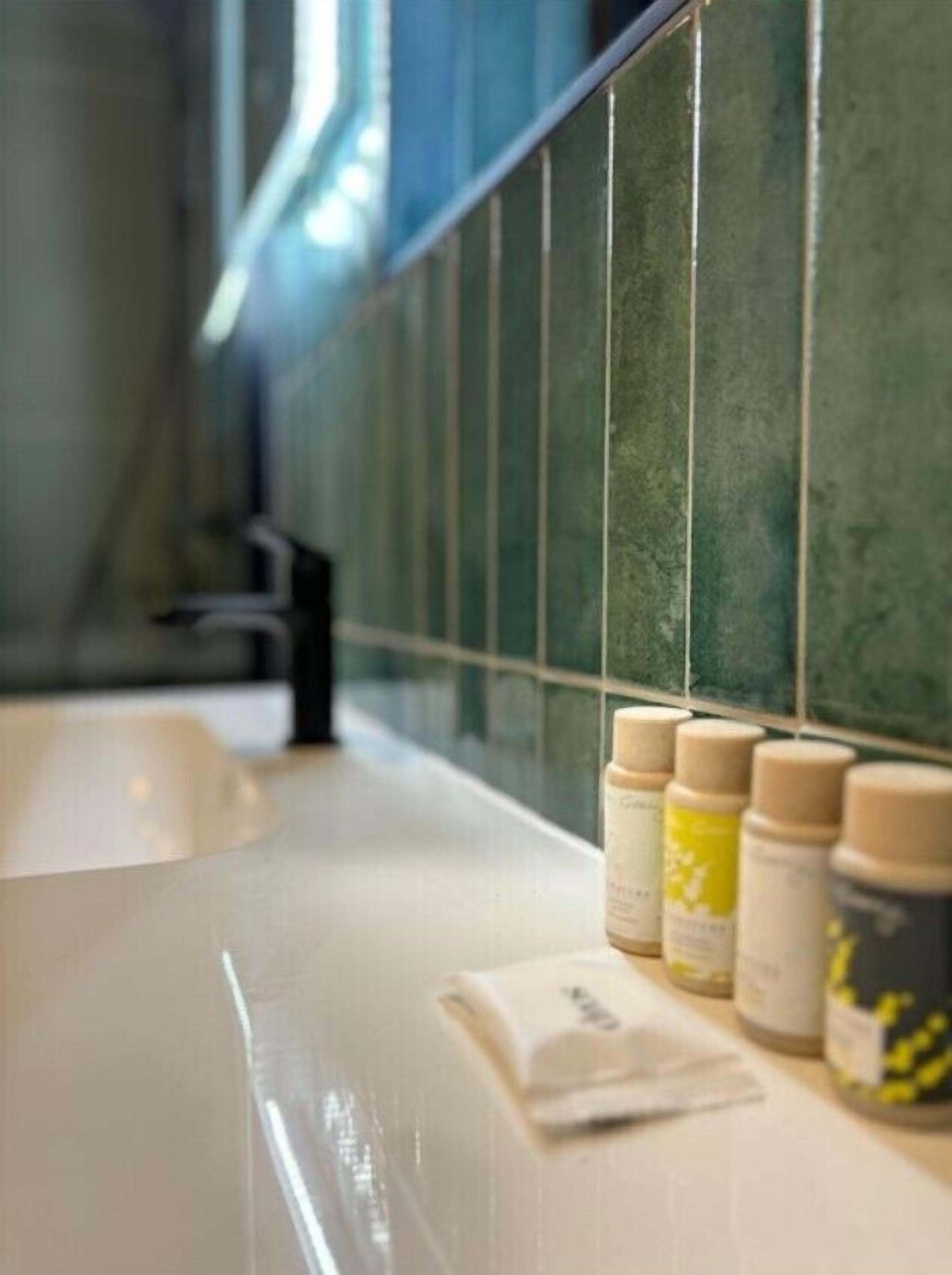 Un baño con un lavabo blanco, paredes de azulejos verdes y un espejo.