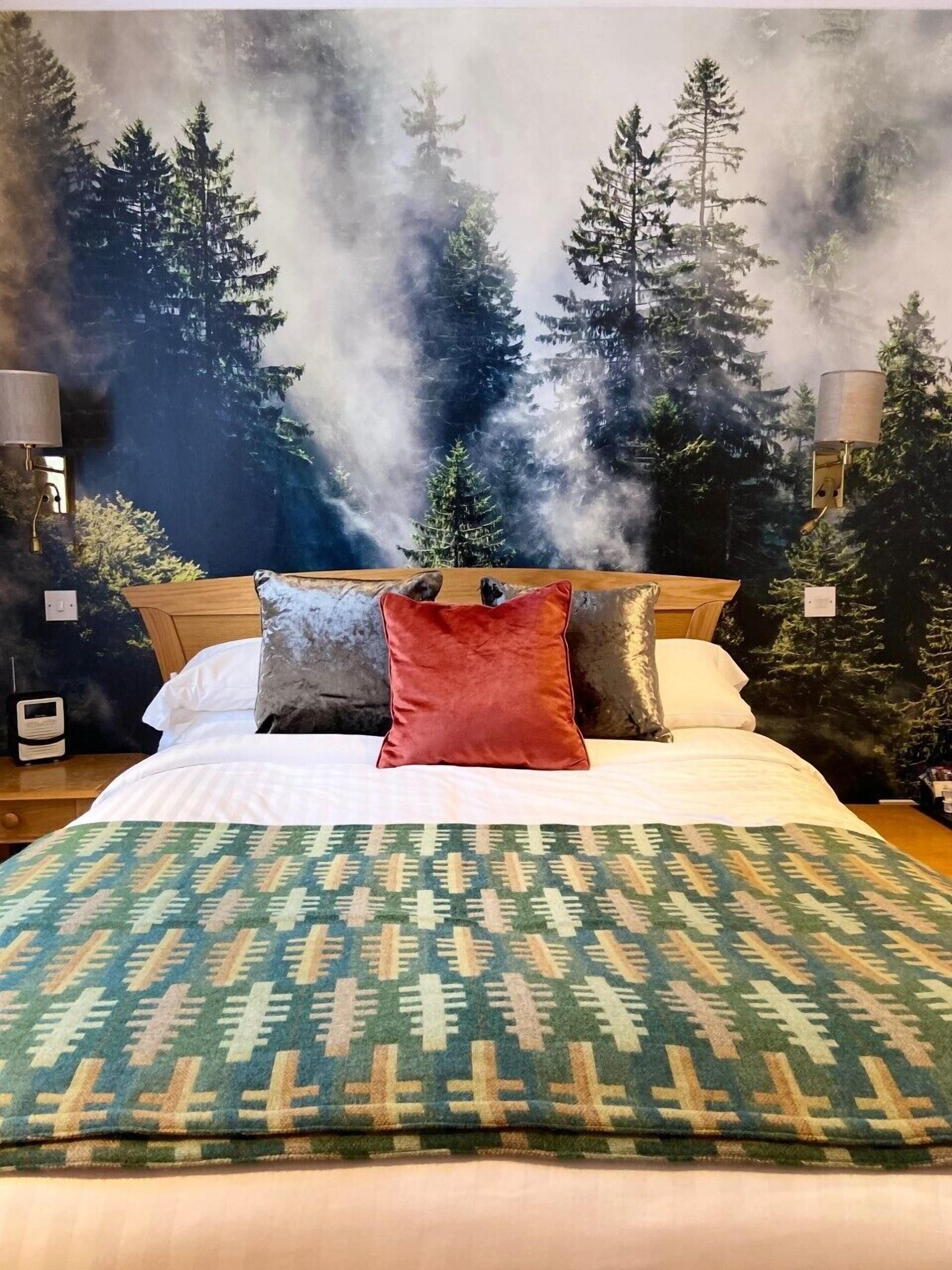 A bed with a patterned blanket, pillows, and a backdrop of a forest scene with smoke.