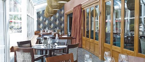 A restaurant with multiple tables and chairs, large windows, and a patterned wall.