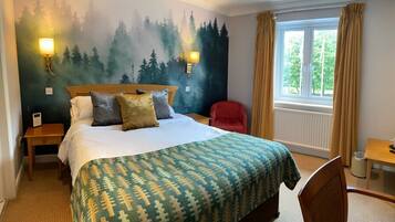 A hotel room with a bed, two wall-mounted lamps, a window with curtains, a small table, and a chair.